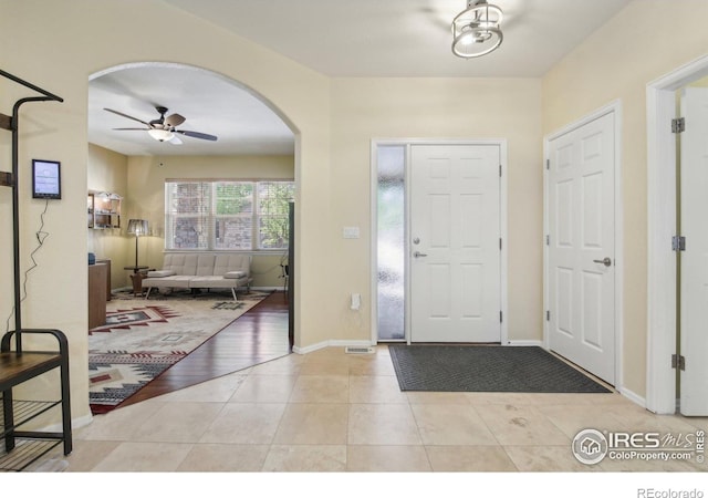 entrance foyer featuring arched walkways, a ceiling fan, baseboards, and light tile patterned flooring