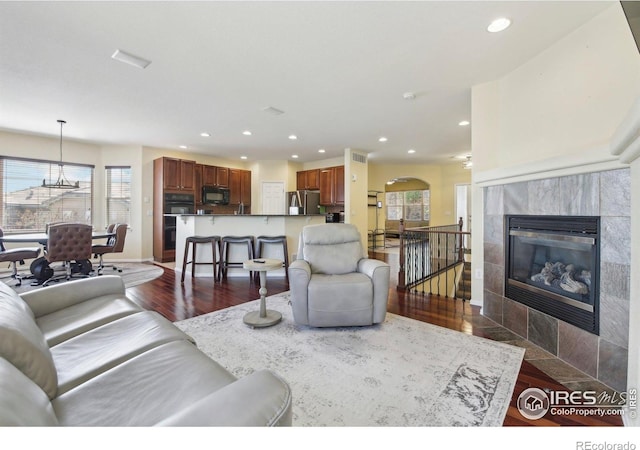 living room featuring dark wood-style floors, recessed lighting, baseboards, a tiled fireplace, and arched walkways