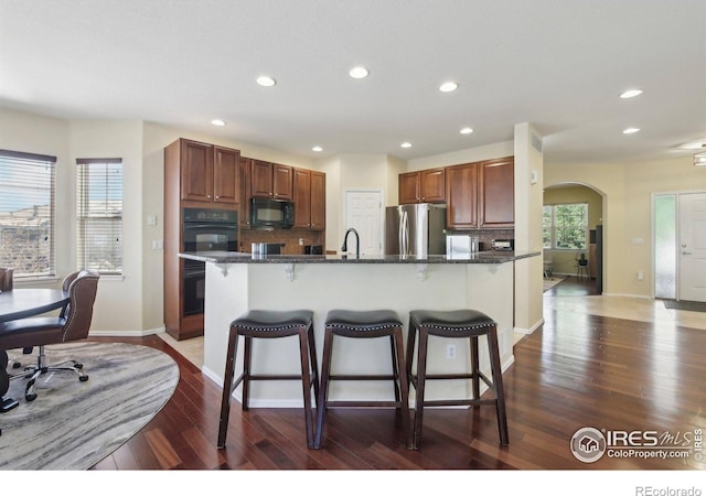 kitchen featuring black appliances, a breakfast bar area, recessed lighting, dark wood-style floors, and arched walkways