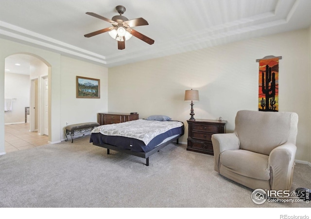 bedroom with arched walkways, a raised ceiling, carpet floors, baseboards, and tile patterned floors
