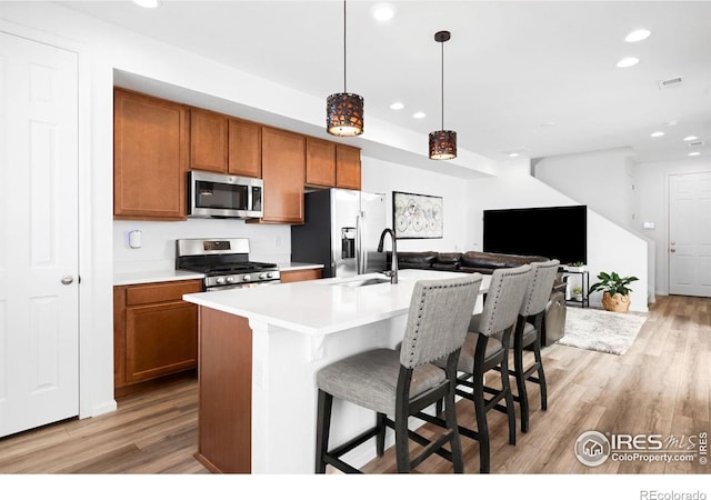 kitchen featuring appliances with stainless steel finishes, light wood-style flooring, recessed lighting, brown cabinetry, and a sink
