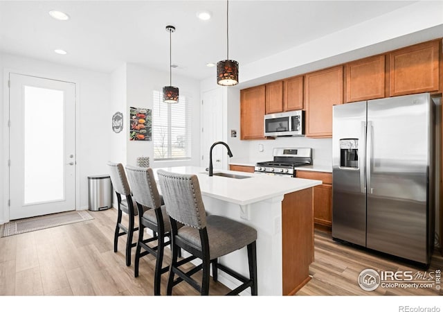 kitchen featuring stainless steel appliances, a sink, brown cabinets, light wood-type flooring, and recessed lighting