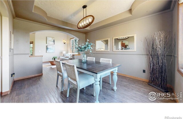 dining area with wood finished floors, arched walkways, a raised ceiling, baseboards, and crown molding