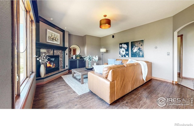 living room with wood finished floors, a glass covered fireplace, arched walkways, and baseboards