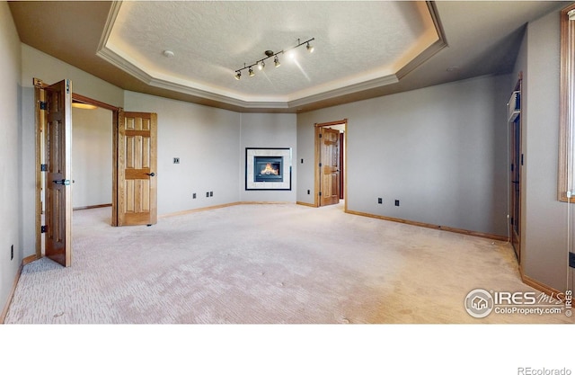 unfurnished bedroom featuring a tray ceiling, baseboards, carpet floors, a glass covered fireplace, and a textured ceiling