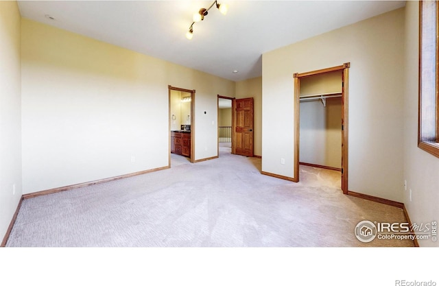 unfurnished bedroom featuring a spacious closet, light colored carpet, and baseboards