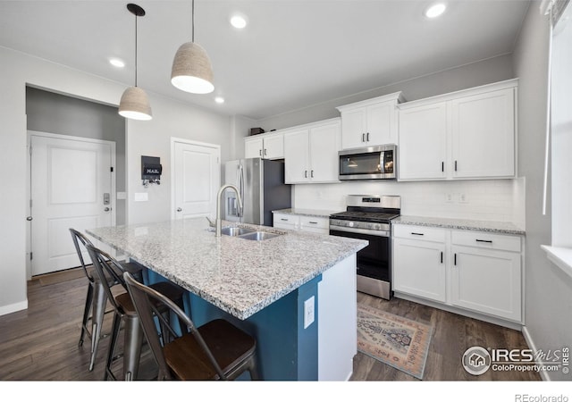 kitchen with stainless steel appliances, a sink, dark wood-type flooring, a kitchen island with sink, and decorative backsplash