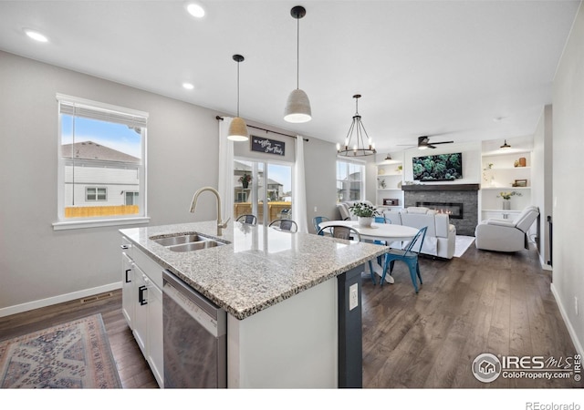 kitchen featuring a sink, stainless steel dishwasher, baseboards, a glass covered fireplace, and dark wood finished floors