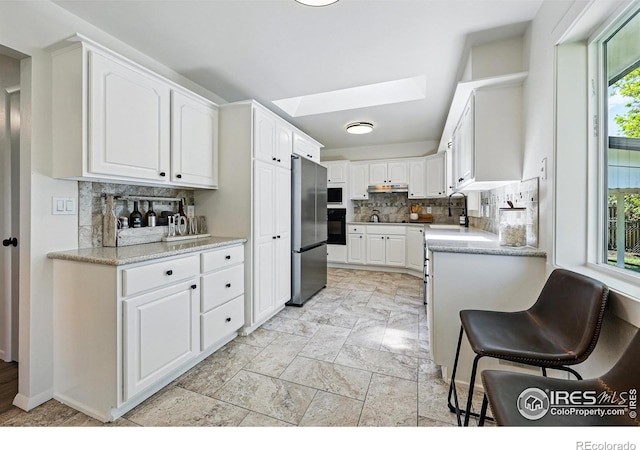 1805 W 22nd St, Loveland, CO 80538 - kitchen with freestanding refrigerator, decorative backsplash, a skylight, white cabinets, and under cabinet range hood