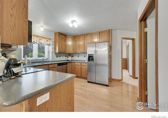 kitchen with appliances with stainless steel finishes, light wood finished floors, dark countertops, a textured ceiling, and a sink