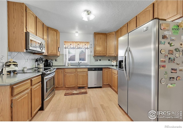 kitchen featuring appliances with stainless steel finishes, light wood-style flooring, tasteful backsplash, a textured ceiling, and a sink