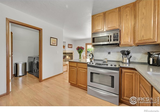 kitchen with appliances with stainless steel finishes, washing machine and dryer, light wood-style floors, tasteful backsplash, and light countertops