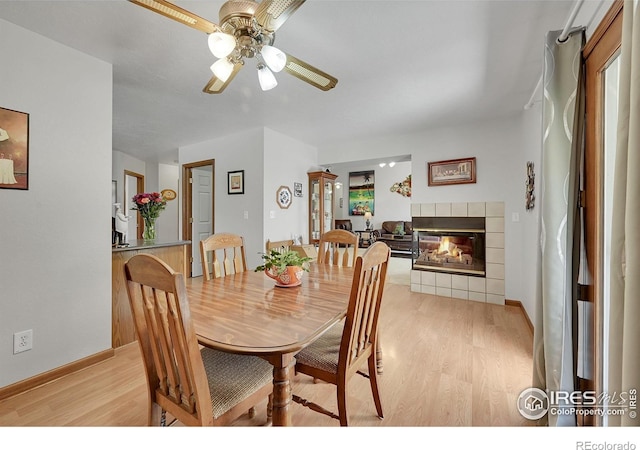 dining room featuring light wood-type flooring, ceiling fan, a fireplace, and baseboards