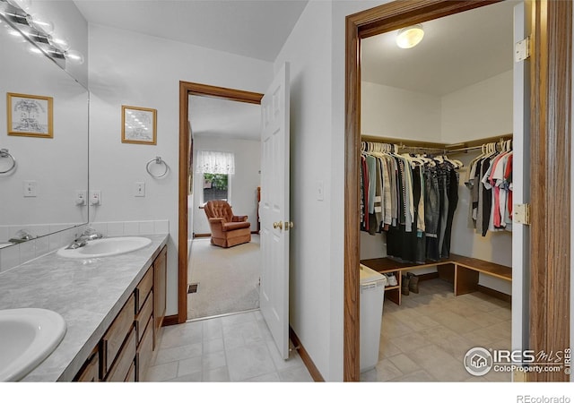 full bathroom featuring double vanity, a spacious closet, and baseboards