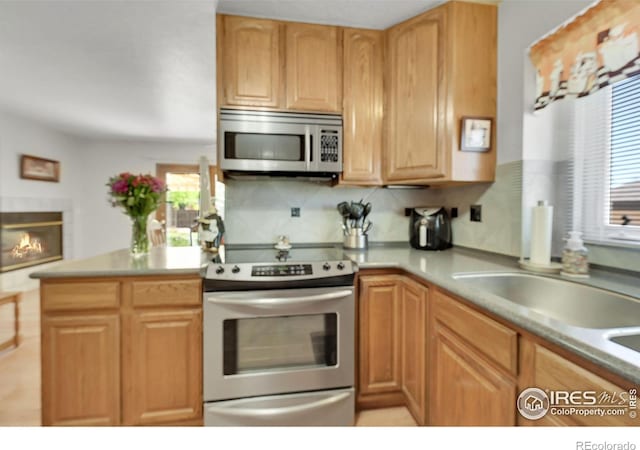 kitchen with appliances with stainless steel finishes, tasteful backsplash, light countertops, and a glass covered fireplace