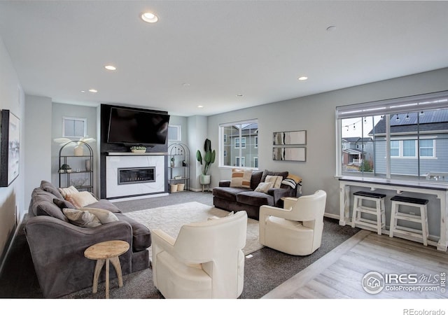 12917 Fox St, Broomfield, CO 80020 - living room featuring healthy amount of natural light, recessed lighting, a glass covered fireplace, wood finished floors, and baseboards