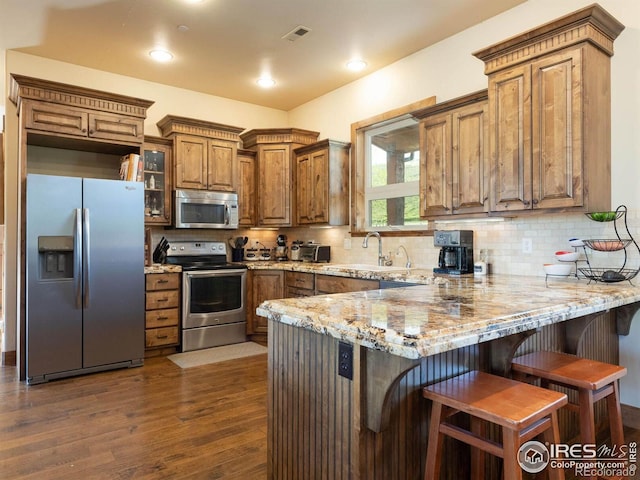 9840 Buckhorn Rd, Loveland, CO 80538 - kitchen featuring appliances with stainless steel finishes, a peninsula, brown cabinets, dark wood-style flooring, and light stone countertops