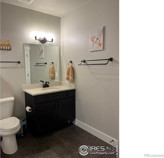 bathroom featuring wood finished floors, vanity, toilet, baseboards, and a textured wall