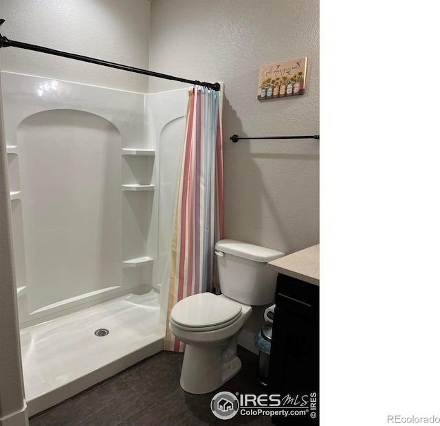 bathroom with a textured wall, a shower stall, toilet, and vanity