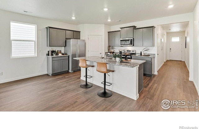 2727 73rd Ave, Greeley, CO 80634 - kitchen featuring appliances with stainless steel finishes, gray cabinets, an island with sink, a kitchen breakfast bar, and recessed lighting