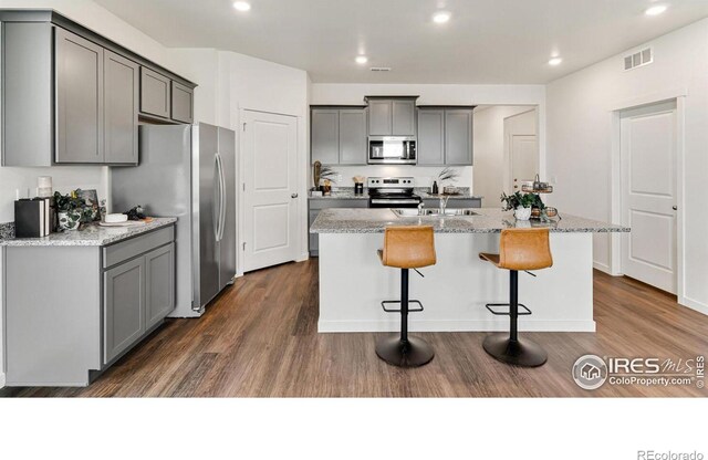 2727 73rd Ave, Greeley, CO 80634 - kitchen featuring stainless steel appliances, gray cabinetry, dark wood-style flooring, a center island with sink, and a breakfast bar