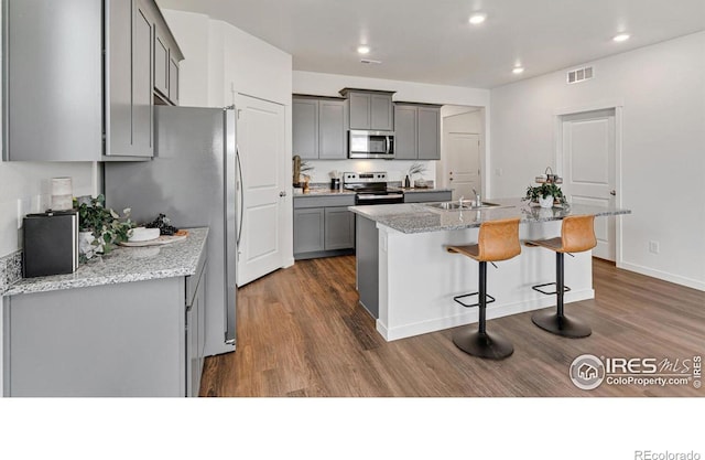 2727 73rd Ave, Greeley, CO 80634 - kitchen with gray cabinets, stainless steel appliances, dark wood-style floors, a sink, and a breakfast bar area
