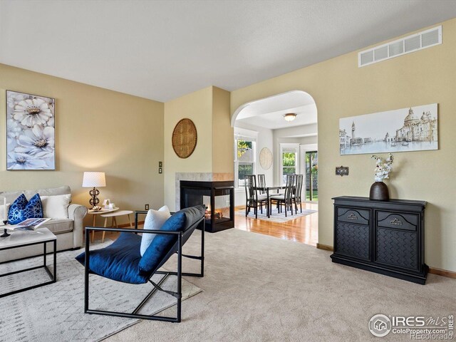 carpeted living area with arched walkways, a multi sided fireplace, and baseboards