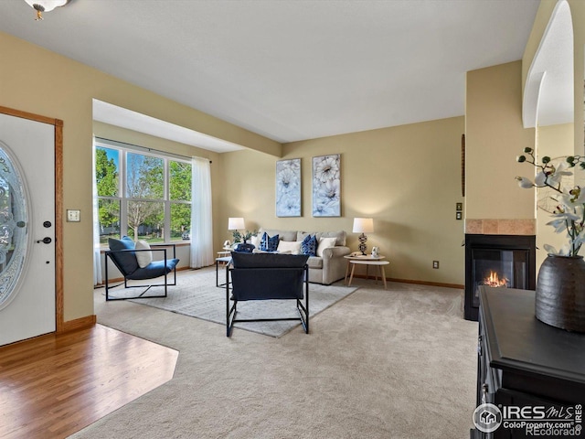 living area featuring a tiled fireplace, baseboards, and light colored carpet