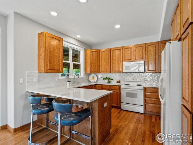 kitchen with white appliances, a peninsula, light wood finished floors, a kitchen bar, and tasteful backsplash