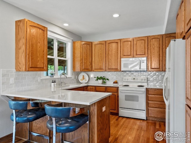 kitchen with white appliances, a sink, a peninsula, a breakfast bar area, and light wood-style floors