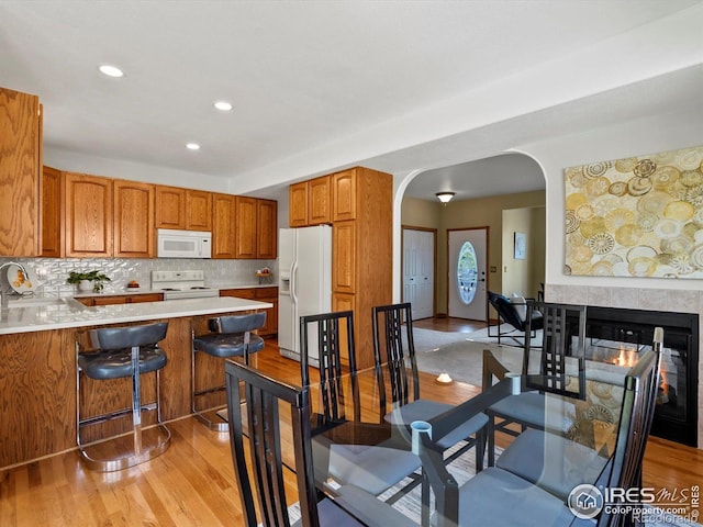 dining room featuring arched walkways, light wood-style floors, recessed lighting, and a multi sided fireplace