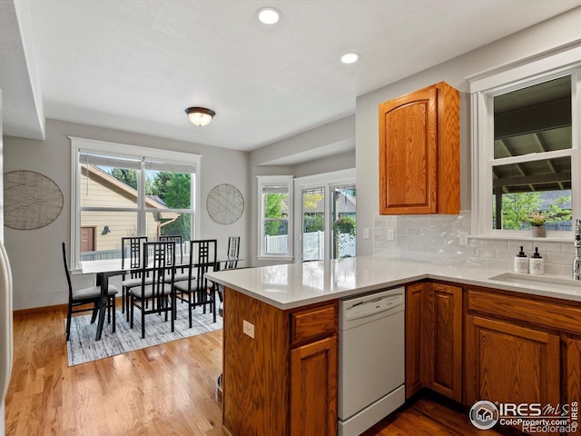 kitchen featuring dishwasher, a sink, brown cabinets, light countertops, and tasteful backsplash