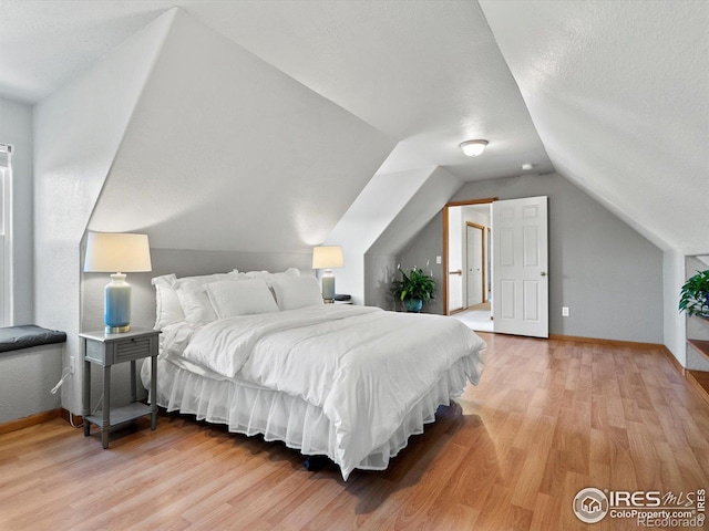 bedroom with light wood-style floors, lofted ceiling, baseboards, and a textured ceiling