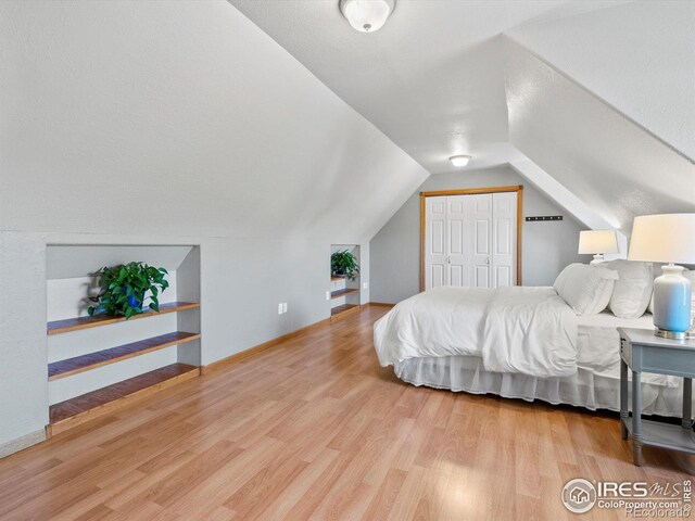 bedroom with wood finished floors, baseboards, a closet, and lofted ceiling