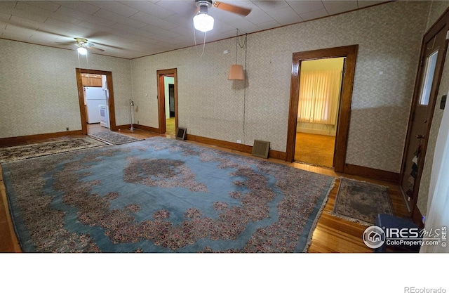 spare room featuring a ceiling fan, wood finished floors, baseboards, and wallpapered walls