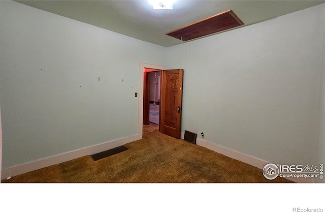 carpeted spare room featuring attic access and baseboards