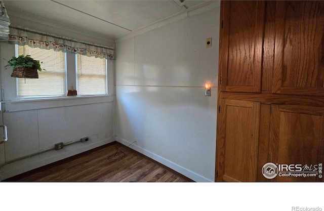 spare room featuring dark wood-style flooring, ornamental molding, and baseboards