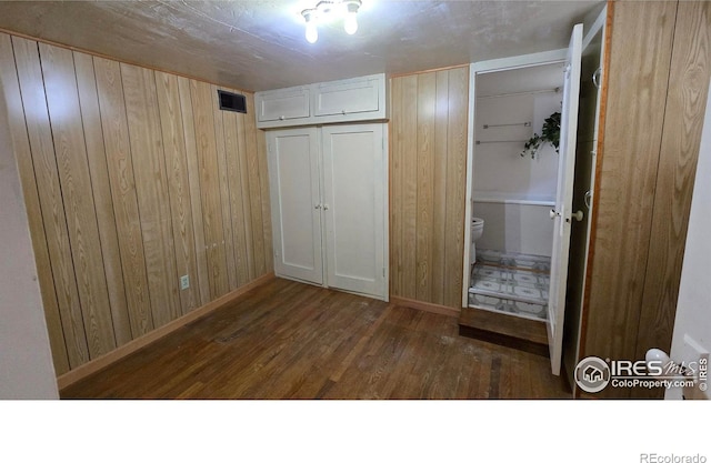 unfurnished bedroom featuring wood finished floors, wooden walls, baseboards, and connected bathroom