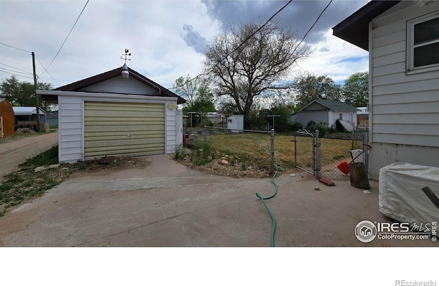 view of patio featuring concrete driveway, fence, a garage, and an outbuilding