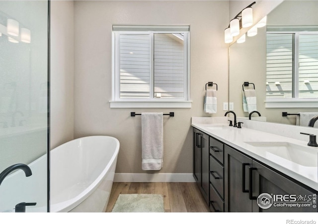 1721 Brightwater Dr, Fort Collins, CO 80524 - bathroom featuring wood finished floors, a freestanding tub, double vanity, and baseboards
