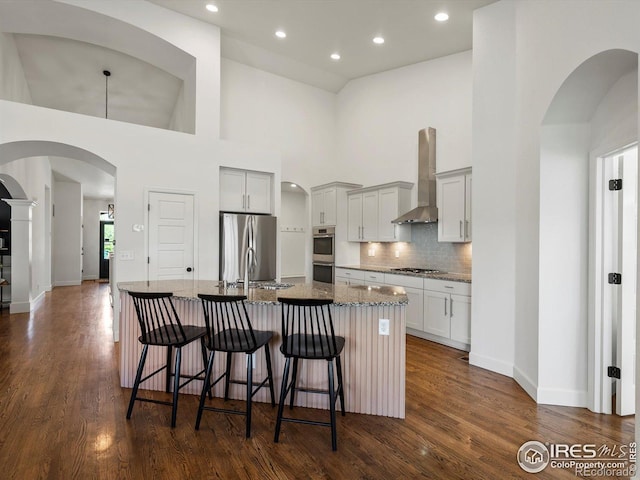 950 Sumner Way, Erie, CO 80516 - kitchen featuring wall chimney range hood, stainless steel appliances, a large island, a high ceiling, and stone countertops
