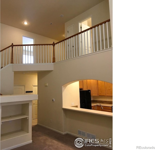 6608 W 3rd St Unit 35-58, Greeley, CO 80634 - unfurnished living room featuring dark colored carpet, baseboards, arched walkways, a towering ceiling, and stairway