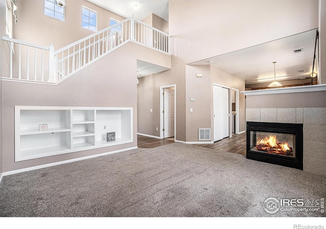 unfurnished living room with carpet floors, a high ceiling, baseboards, a fireplace, and stairs