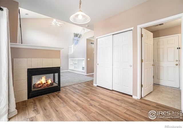unfurnished living room with a tiled fireplace, wood finished floors, a ceiling fan, and baseboards