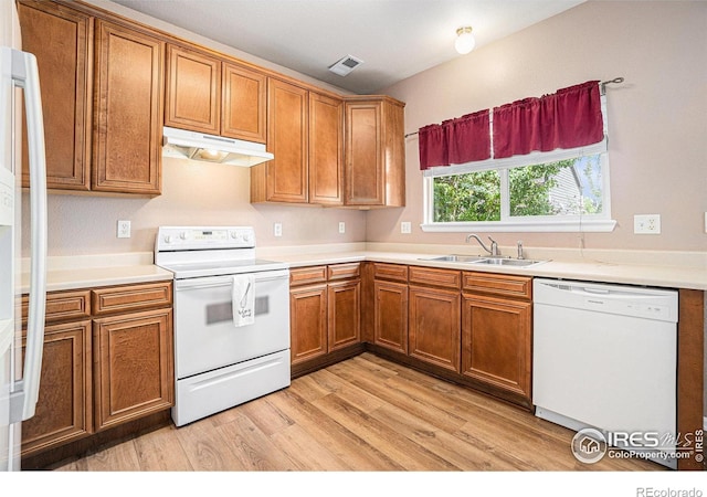 kitchen featuring white appliances, under cabinet range hood, a sink, and brown cabinets