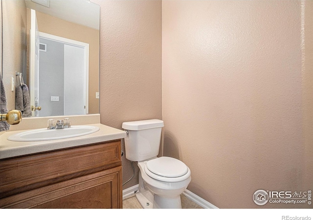 bathroom with vanity, a textured wall, toilet, and baseboards