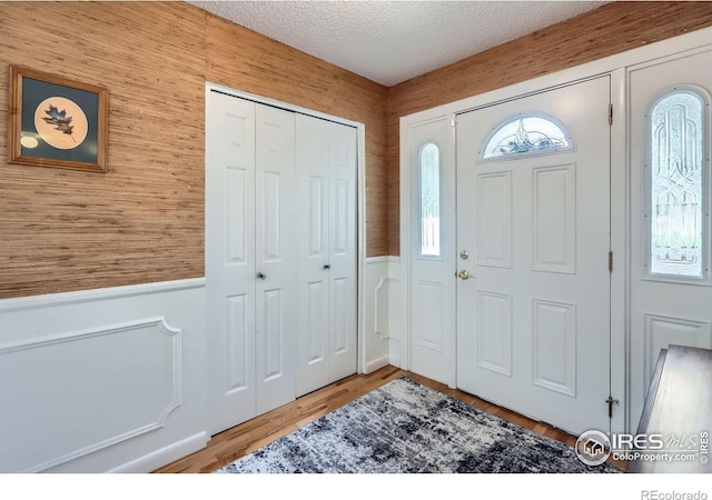 foyer with a wainscoted wall, a textured ceiling, and wood finished floors