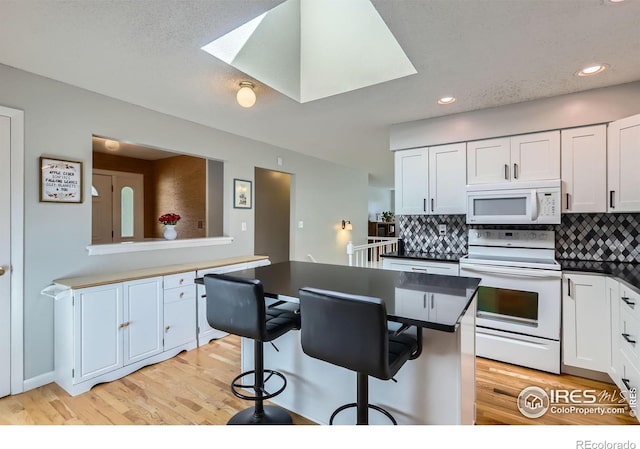 kitchen with white appliances, backsplash, light wood finished floors, a kitchen bar, and white cabinets