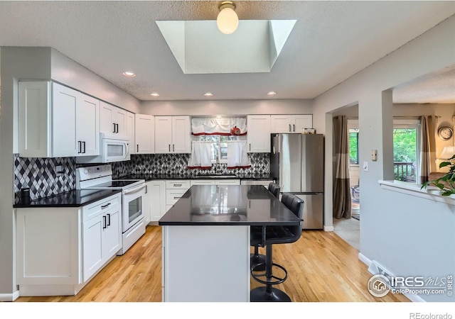 kitchen featuring white appliances, a kitchen breakfast bar, dark countertops, white cabinets, and recessed lighting