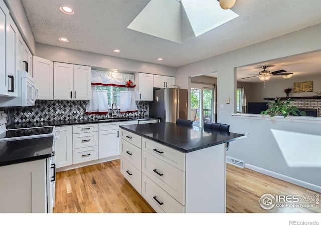 kitchen with a sink, dark countertops, white microwave, freestanding refrigerator, and light wood-style floors